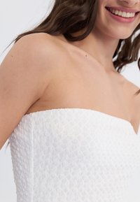 Weißes trägerloses Kleid mit einem strukturierten Diamantmuster, das einen taillierten Oberteil und eine glatte Oberfläche betont. Einfaches und elegantes Design.