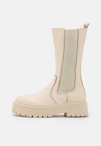 Botas de tobillo beige con un cuerpo de cuero texturizado, paneles laterales elásticos y una suela de plataforma gruesa con un diseño de banda de rodadura resistente.