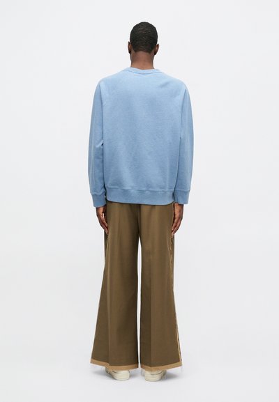 Sudadera de color azul claro con mangas raglán, cuello redondo y tejido texturizado; combinada con pantalones anchos marrones que presentan un detalle lateral en contraste.