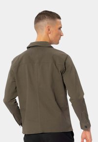 Olivengrøn langærmet skjorte med standard krave, rygsygning og knapmanchetter. Fremstillet af en struktureret stofkvalitet med et tætsiddende design.