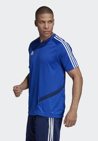 Blaues Sport-Shirt mit kurzen Ärmeln, das weiße vertikale Streifen an den Schultern und einen marineblauen Akzent an der Seite aufweist. Hergestellt aus leichtem Stoff.