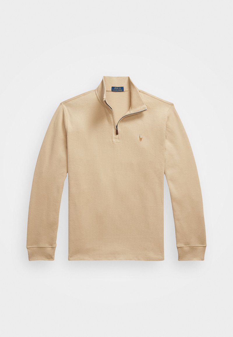 Polo shirt beige à manches longues avec col zippé, fabriqué en tissu texturé, portant un petit logo brodé sur la poitrine gauche.