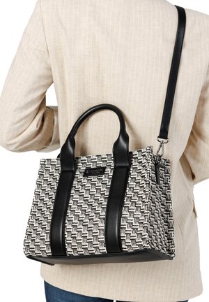 Personne portant un blazer beige avec un sac à main tissé noir et blanc, doté de poignées en cuir noir et d'une bandoulière amovible.