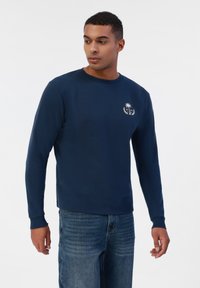 Sweatshirt bleu marine à manches longues en mélange de coton avec col rond, présentant un petit logo blanc de palmier sur la poitrine et des poignets côtelés.