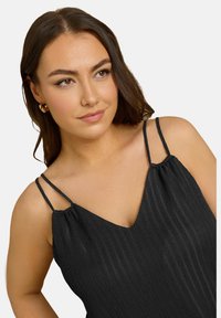 Musta hihaton toppi texturoitumat fabricilla, jossa on ohuet säädettävät nauhat ja V-aukko. Materiaalissa on hienovaraisia pystyridgejä.