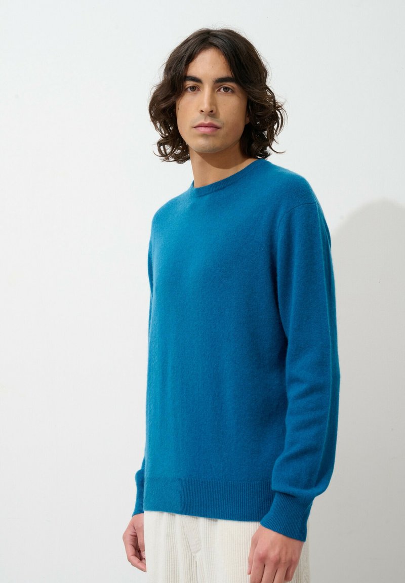 Pull bleu en tricot doux, doté de manches longues, d'un col rond et de poignets et ourlet côtelés.