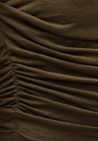 Közelkép olívazöld szövetről, amelyen vízszintes gyűrődések texturált redőket és fodrokat hoznak létre a felületen.