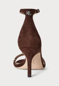 Bruna mockaskinnsandaler med hög klack, med en smal ankelrem, öppen tå-design och silverfärgad logotypaccent på klacken. Mjuk textur, spetsig form.