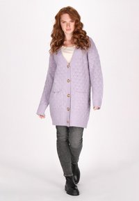 Cardigan lavorato a maglia di un leggero colore lavanda con motivo a diamante, chiusura con bottoni, tasche e maniche lunghe, abbinato a jeans grigi scuri e stivali neri.