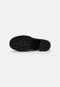 Sole di scarpa in gomma nera con un motivo di presa testurizzato, caratterizzato da scanalature orizzontali e verticali per trazione e stabilità.