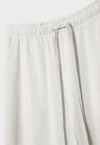 Gros plan de la ceinture d’un pantalon en lin beige clair avec bande élastique et lien noué.