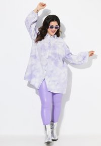 Maglietta oversize color lavanda con effetto tie-dye e bottoni, abbinata a leggings lucidi color lavanda e stivaletti argento. Il tessuto ha un aspetto strutturato.
