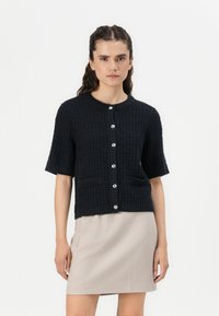 Zwarte, textuurgebreide cardigan met korte mouwen, geribbelde halslijn en knoopsluiting aan de voorkant. Beschikt over twee voorzakken voor extra detail.