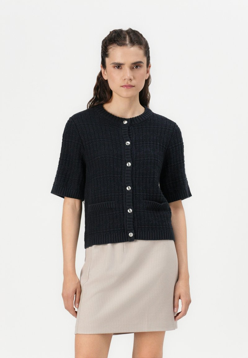 Zwarte, textuurgebreide cardigan met korte mouwen, geribbelde halslijn en knoopsluiting aan de voorkant. Beschikt over twee voorzakken voor extra detail.