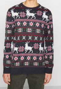 Marinblå stickad tröja med vita renar, snöflingor och diamante mönster i rött och grönt. Rund halsringning med ribbade ärmslut och nederkant.