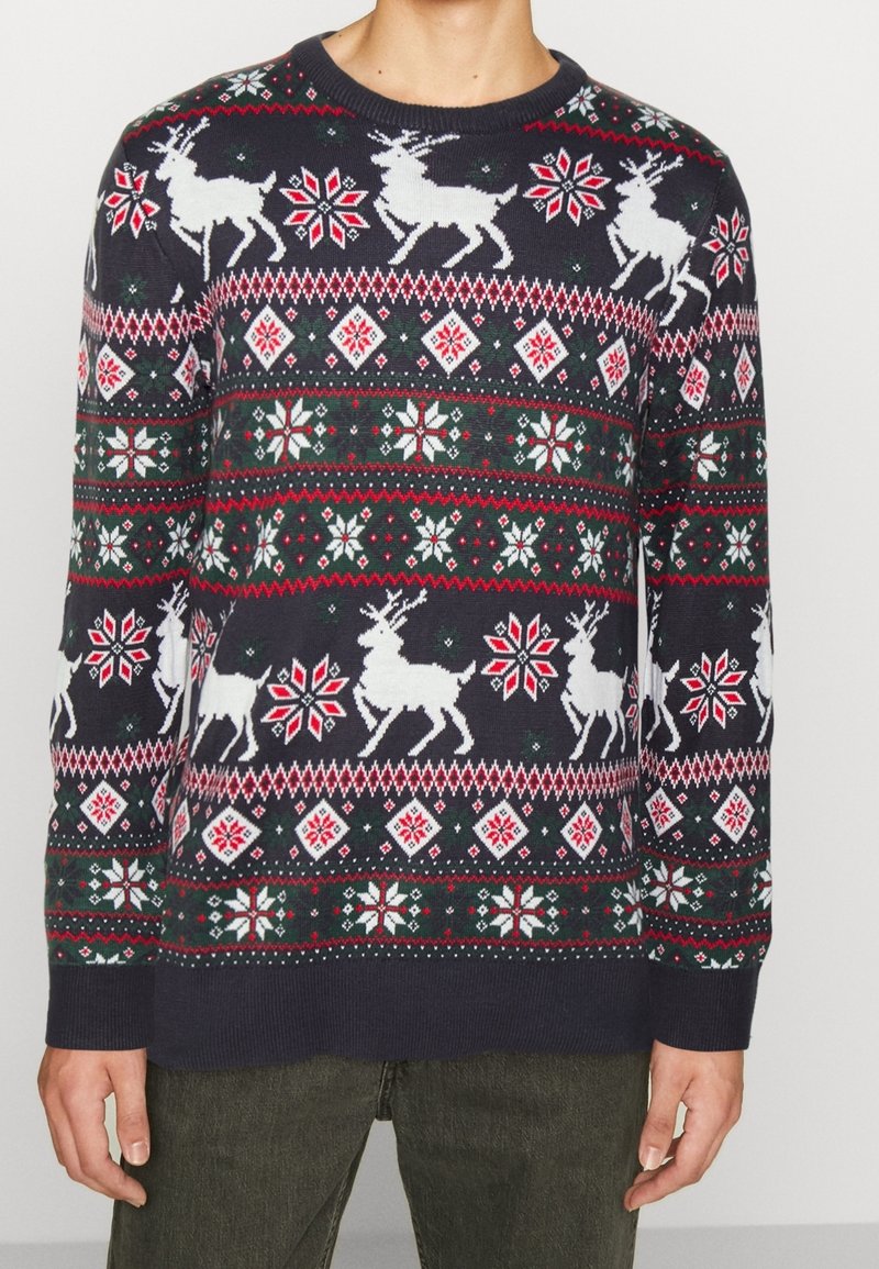 Marinblå stickad tröja med vita renar, snöflingor och diamante mönster i rött och grönt. Rund halsringning med ribbade ärmslut och nederkant.