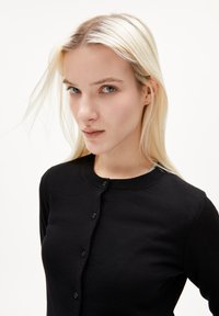 Svart cardigan i stickad kvalitet, med rund hals och knappstängning fram. Slät yta med en kroppsnära design.