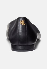 Ballerine in pelle nera con finitura liscia, suola piatta e emblema dorato sul tallone. Presentano una punta arrotondata e un design minimalista.