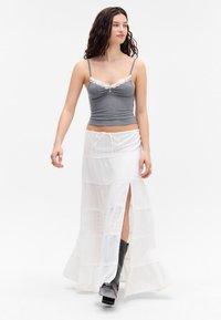 Débardeur gris à côtes avec bordure en dentelle ; jupe maxi blanche superposée avec des motifs œillets et fente latérale ; bottes noires à talons.