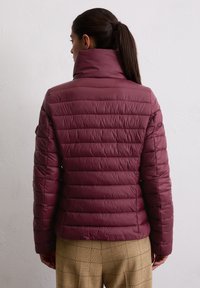 Bordeaux pufferjack met hoge kraag, geborduurd patroon en aansluitend ontwerp, gecombineerd met geruite broeken in een neutrale kleur.