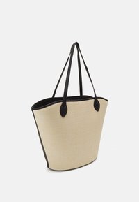 Tote-väska i strukturerat beige material med svarta läderdetaljer och handtag, med en bred, avsmalnande form.