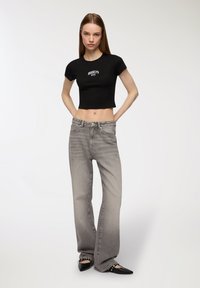 Maglietta nera corta con la scritta "BROOKLYN NYC", jeans grigi a campana con design sbiadito e ballerine nere a punta con dettagli borchiati.