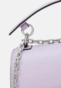 Fialová kožená taška s texturou, která má stříbrný řetězový popruh, černé lemování a kovový kroužek pro zvýšení detailu.
