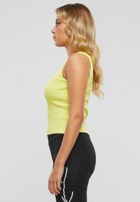 Gul stripet tanktopp med tettsittende design, kombinert med høyt liv svarte leggins med hvite dekorative sømmer.