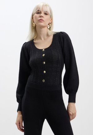 Maglione nero lavorato a maglia con scollo a barca, maniche lunghe a sbuffo e bottoni dorati sul davanti. Motivo testurizzato e vita aderente.