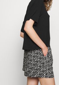 Zwart T-shirt met korte mouwen, gecombineerd met zwart-crème korte broek met patroon, voorzien van zakken en een ontspannen pasvorm.