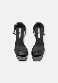 Svarta lackläder högklackade sandaler med öppen tå, ankelrem och en bred framrem. Texturerade innersulor och en fyrkantig häldesign.