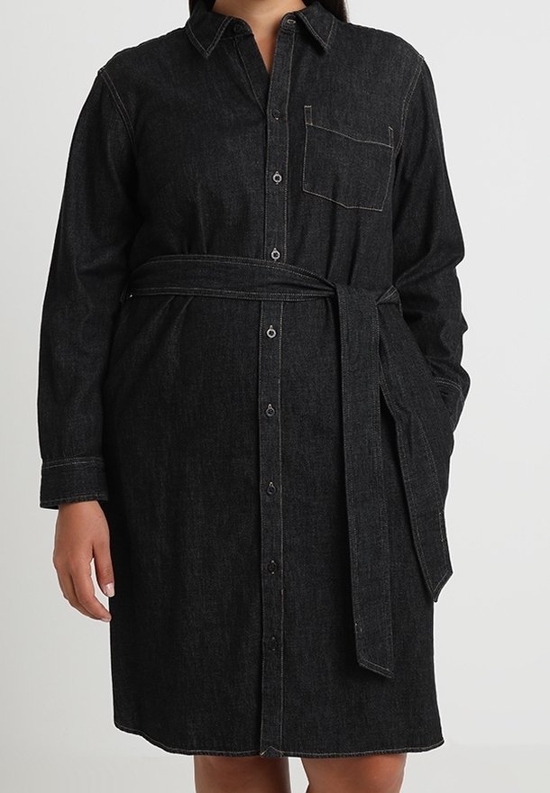 Černé džínové šaty s dlouhým rukávem, předními knoflíky, náprsní kapsou a odpovídajícím páskem ze stejné látky zavázaným v pase.