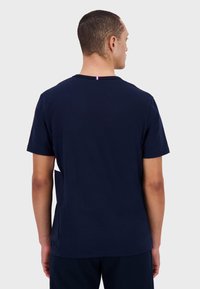 T-shirt en coton bleu marine à manches courtes, col rond et avec un petit accent rouge, blanc et bleu au dos du col.