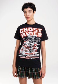 Black cotton T-shirt featuring a Ghost Rider graphic with red and white text. The shirt has a crew neckline and is paired with a plaid skirt.