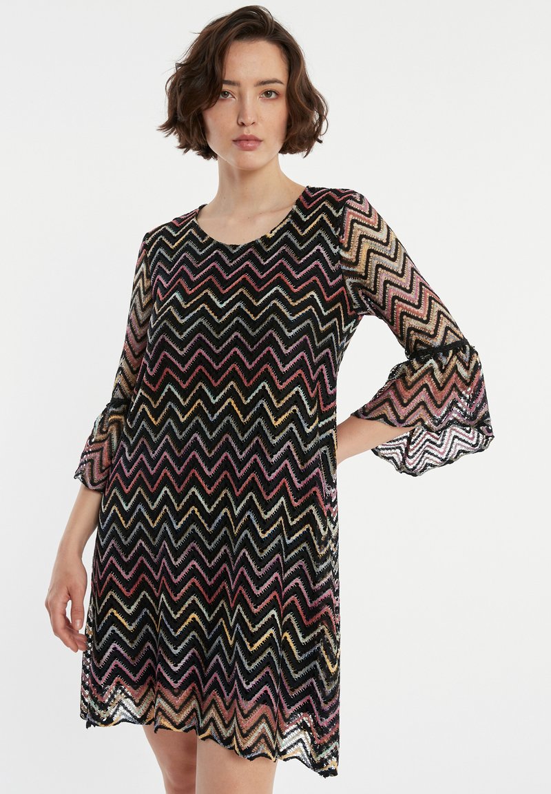 Robe noire à motifs zigzag avec un matériau transparent, des manches évasées trois-quarts et un décolleté rond. Comprend des rayures multicolores sur l'ensemble.