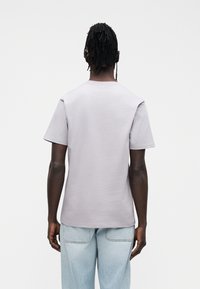 T-shirt cinzenta clara de manga curta com decote redondo, feita de tecido macio, mostrada de costas, combinada com jeans azul claro.