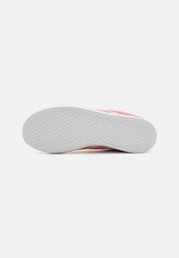 Schuhsohle mit Sechseck- und Sternmuster-Profil, zeigt die weiße Unterseite und den teilweisen pinken oberen Teil vor einem schlichten weißen Hintergrund.
