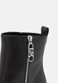 Bottine en cuir noir avec fermeture éclair argentée et tirette logo "ZARA", dotée d'une boucle en haut pour un enfilage facile.