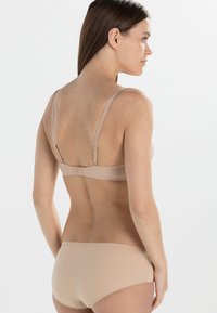 Beige trådløs bh med justerbare tynne stropper og kroklukking, kombinert med matchende sømløse bikinibokser. Glatt stoffstruktur.