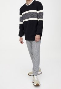 Pull en maille bleu marine avec des rayures blanches, associé à un pantalon à carreaux gris et des baskets beiges. Tissu texturé et coupe décontractée.