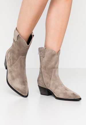 Bottines en daim tan avec un bout pointu, une fermeture éclair sur le côté et un petit talon empilé, présentant un design légèrement souple et des coutures minimalistes.