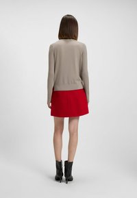 Beige ribattu neule, jossa on vartalonmyötäinen muotoilu, yhdistettynä punaiseen pörröiseen hameeseen. Mallilla on päällään mustat nilkkurit, joissa on vetoketjukiinnitys.