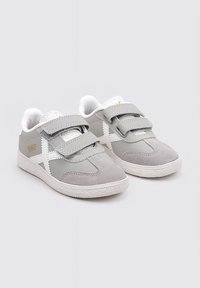 Zapatillas de velcro grises con materiales de ante y sintéticos, que presentan acentos blancos y una suela de goma texturizada. Punta redondeada y interior acolchado.