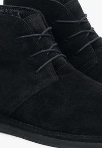 Czarne zamszowe botki za kostkę z okrągłymi sznurówkami, teksturowanym materiałem i gładką gumową podeszwą. Minimalistyczny design z subtelnymi detalami w szyciu.