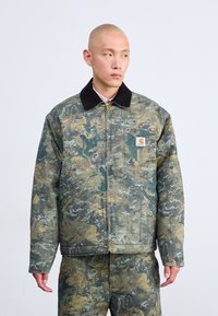 Giacca dal motivo camouflage con zip frontale, colletto nero e tasche laterali, dotata di una patch con logo sul petto e una vestibilità rilassata.