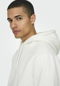 Weißer Hoodie mit Kordelzug, lockere Passform, aus glattem Stoff gefertigt. Verfügt über eine große Kapuze und ein einfaches, klares Design.