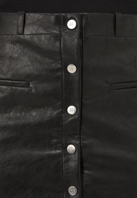 Jupe en similicuir noire avec boutons-pression argentés à l'avant gravés du logo DKNY et deux poches fendues horizontales.