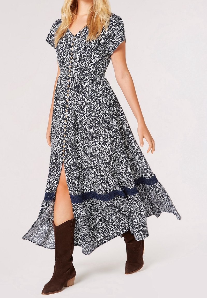 Femme portant une robe midi tachetée noir et blanc avec des boutons sur le devant et des bottes hautes en daim marron.