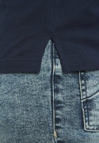 Marineblaues Baumwoll-T-Shirt mit seitlichem Schlitz, kombiniert mit hellblauen Denim-Jeans mit strukturiertem Muster und sichtbaren Nahtdetails.