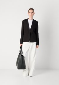 Blazer nero con vestibilità aderente, chiusura a un bottone e due tasche frontali, abbinato a pantaloni bianchi a gamba larga e una borsa in pelle nera.